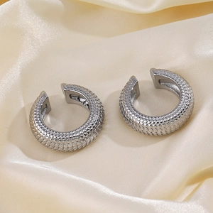 Silver stainless steel ear cuffs with fish scale texture on a beige silk background