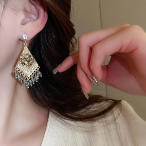 Close-up of gold diamond-set rhombic earrings with deep blue beaded tassels