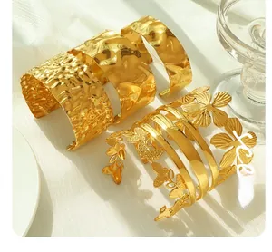 Detail of four gold oversized textured bangles with hammered patterns and floral accents
