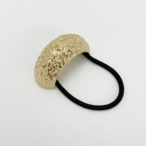 Detail of a matte gold U-shaped metal hair tie with a textured finish and black elastic band