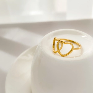 Detail of interlocking golden heart rings displayed on a minimalist white ceramic base