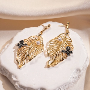 Macro shot of gold leaf earrings with white pearls and black butterfly details on stone