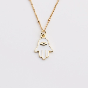 Macro view of gold Hamsa Hand necklace pendant with white enamel and eye detail