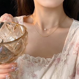 Close-up of double-layered gold necklace with baroque pearl on elegant female model