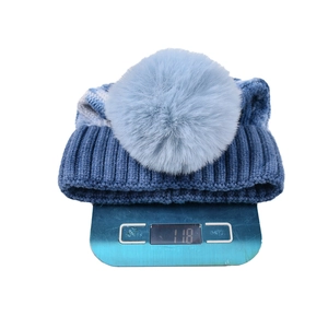 Detailed view of tie-dye knit beanie with faux fur pom pom on an electronic scale