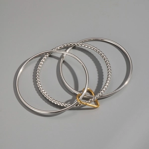 Macro detail of layered stainless steel rings and gold heart charm in silver finish