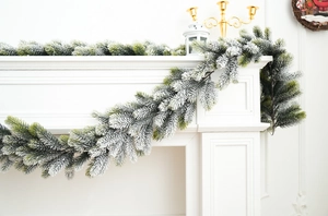 Detail of flocked Christmas garland with snow-covered pine needles on white fireplace