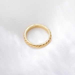 Detailed macro shot of a gold-plated S925 silver twist ring on white silk background