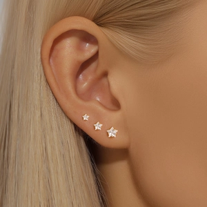 Detailed view of three gold star stud earrings with white zircons on a model's ear
