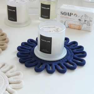 Detail of dark blue flower shaped braided cotton trivet with soy wax scented candle