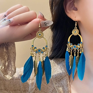 Detail of bohemian gold feather earrings featuring blue beads and metal leaf pendants