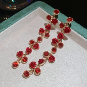 Detailed close-up of red rose petal tassel earrings with sparkling crystals in a velvet box