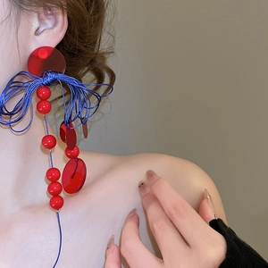 Detailed shot of long geometric dangle earrings with blue woven knots and red beads