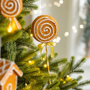 Gingerbread candy ornament with yellow bow hanging on a festive Christmas tree