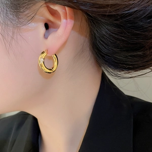 Detail of a gold plated thick hoop earring featuring a single round cubic zirconia stone