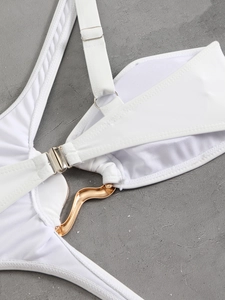 Detail of white swimsuit with gold wave buckle and adjustable strap on grey background