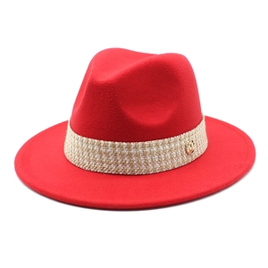Detail of red wool fedora hat featuring woven band and gold M emblem on a white background