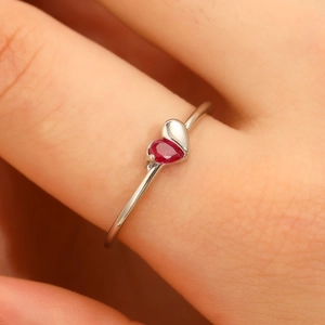 Macro shot of minimalist silver ring featuring a heart-shaped red gemstone and polished metal