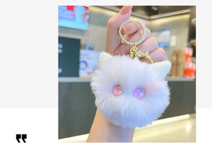 Close-up of a white plush kitten keychain with sparkling pink eyes and gold hardware