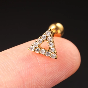 Macro shot of a gold triangle zircon cartilage stud held on a fingertip with black background