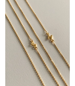 Close-up of golden S and H initial letter pendants on minimalist fine chain necklaces