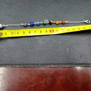 Detalle de pulsera de plata con siete cuentas de colores medida con una cinta métrica amarilla
