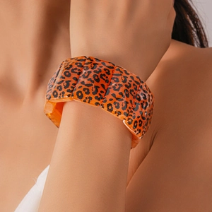 Close-up of a wide chunky orange acrylic bracelet featuring a black leopard print design