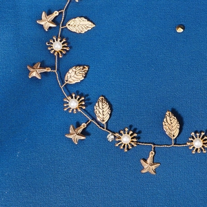 Golden bridal hair vine with starfish, leaves, pearls, and rhinestones on blue background