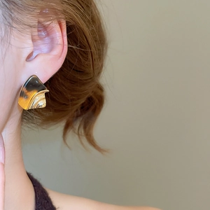 Detail of amber resin geometric earrings with gold-plated finish on model's ear