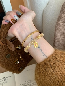 Détail d'un bracelet de perles avec breloque dorée et bracelet zircon au poignet