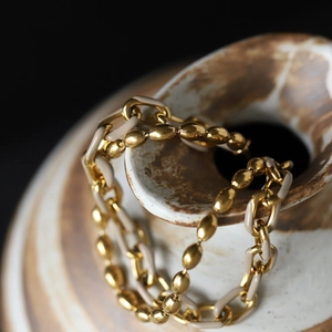 Détail du bracelet chaîne en émail kaki et billes dorées sur un vase en céramique