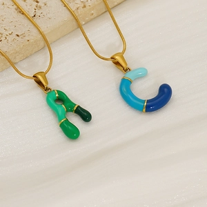 Colorful resin alphabet pendants on gold titanium chains over silk and stone background