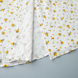 Gros plan d'une robe en coton blanc au motif floral jaune et texture froissée douce