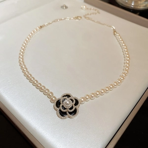 Detail of flower necklace featuring black camellia pendant with pearl center in jewelry box