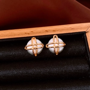 Detail of gold-plated geometric earrings featuring white pearls in a crisscross metal frame