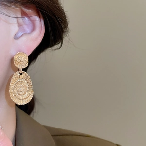 Close-up of golden textured oval drop earrings featuring spiral engraved metal details