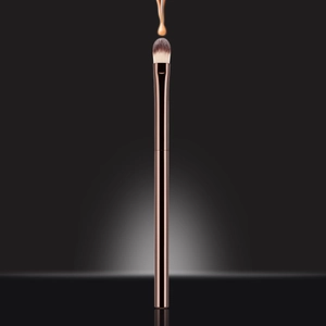 Detail of foundation liquid dripping on a synthetic concealer brush with rose gold handle