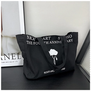 Detail view of black canvas tote bag featuring white floral print and artistic lettering
