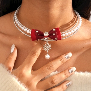 Detail view of a multi-layer snowflake choker with red bow and pearls worn by a model