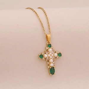 Macro detail of a gold-plated cross necklace with green emerald-cut stones and pearls
