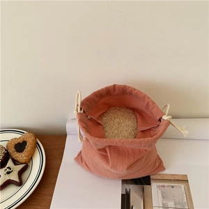 Brick red canvas drawstring storage bag with thick cotton ropes on a wooden table