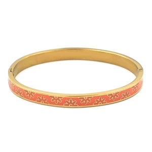 Detail of coral orange enamel flower pattern on a polished gold stainless steel bangle