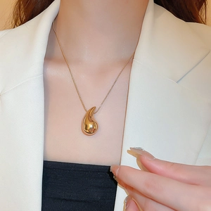 Close-up of golden teardrop pendant necklace worn on a model with white blazer