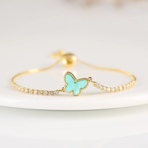 Detail of gold chain bracelet featuring a green butterfly charm and white zircon stones