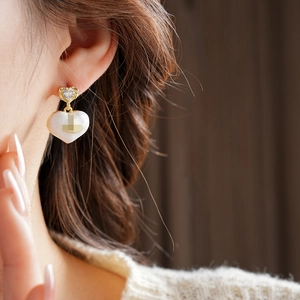 Detail of a model wearing gold-plated heart earrings with white enamel and clear zircons