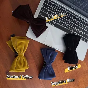 Four velvet bow hair clips in dark coffee, yellow, blue, and black on a wooden desk