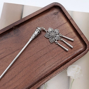 Detail of vintage silver hair pin with floral pendant and tassels on a wooden tray