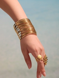 Detail of multi-layer gold bangle stack with sunburst ring on a blue water background