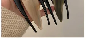 Macro detail of glossy acetate hair clips in black, marble cream, and olive green colors