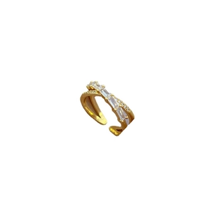 Crossed golden open ring with sparkling rectangular zircons on a clean white background